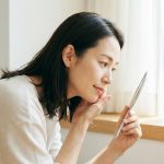 鏡で頬の毛穴を確かめる40代の女性(イメージ)
